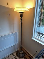 Full view of lit torchiere lamp beside window