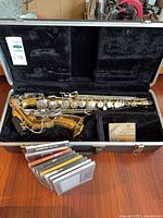 Saxophone in open case with reed box and CDs in front