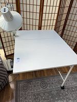 Top view of white folding work table with clamp lamp attached