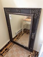 Full view of rectangular ornate framed mirror leaning against wall