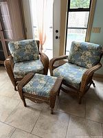Two resin wicker chairs and ottoman with blue floral cushions displayed together
