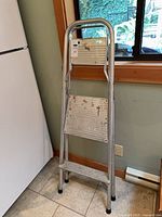 Full view of folded 2-step ladder leaning against wall