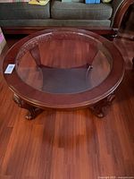 Full view of round coffee table showing glass top, wood frame and legs