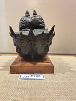 Front view of bronze four-face Buddha head on wooden base