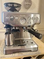 Front and left side view of Breville Barista Express with portafilter, milk pitcher, controls and gauge visible