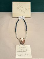 Full view of necklace showing pendant, bead strand and designer info card