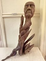 Full view of the wood sculpture with male head emerging and metal figure at base