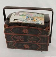 Front view showing lacquered wood tiers, porcelain panel on lid, handle