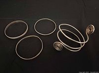 All four silver bracelets laid out on black background