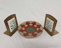 Front view of pair of brass enamel bookends flanking round cloisonné dish