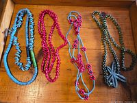 Four necklaces laid out: blue disk beads, pink chip beads, blue with red flowers, green with dragonfly