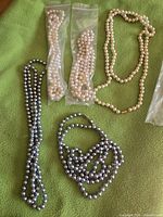 Five assorted faux pearl bead necklaces on green fabric