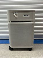 Front view of Austin air purifier showing control knob, brand badge, grille and casters