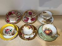 All six teacup and saucer sets arranged, showing patterns and condition