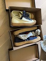 Both shoe boxes opened showing off-white size 8 pair and navy blue size 9 pair.