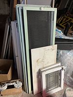 Stack of pale green screen frames, white storm sash with metal grille and additional components