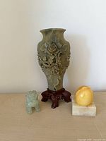 Front view of three stone items: vase on stand, lion, sphere on base
