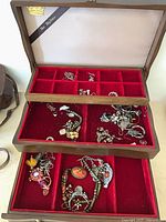 Jewelry box open with two sliding drawers extended showing red velvet compartments and assorted jewelry pieces