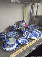 Full group shot of all twelve blue-and-white transferware pieces on shelf with rulers for scale
