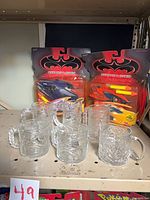 Two sealed action-vehicle sets and six glass mugs on shelf