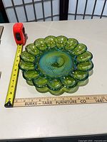 Top view of green carnival glass deviled egg platter with tape measure showing diameter