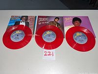 Front view of three red vinyl singles with sleeves displayed