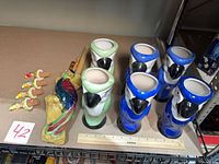 Six parrot tiki mugs, four parrot cork stoppers, ceramic parrot wall decor with wooden flutes displayed on shelf