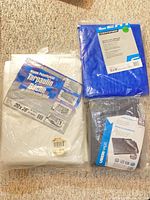 Three packaged tarps: white, blue, black