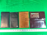Four wallets side by side with ruler for scale; burgundy wallet open showing calculator