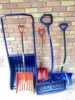 All four snow shovels and snow scoop against brick wall