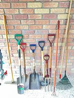 Group of garden tools lined against wall showing full assortment