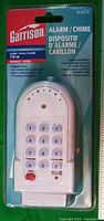 Front of sealed package showing alarm unit, keypad, model info and features
