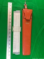 Slide rule front with metal cursor, metric ruler for scale, leather case closed