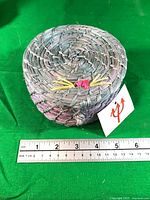 small woven straw basket with lid showing whiskers and pink nose beside ruler