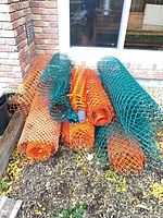 Multiple rolled orange and green plastic mesh fences stacked outdoors