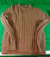 Brown cable-knit V-neck sweater laid flat
