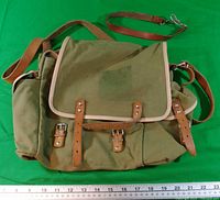 Front of olive drab canvas rucksack with leather straps, ruler for scale