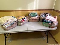 Five grocery bags filled with assorted folded fabrics and linens on table
