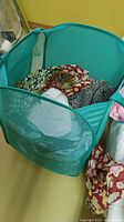 Teal collapsible mesh hamper showing cylindrical shape, wire frame support, mesh sides, and handles