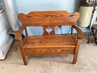 Front view of oak bench showing heart cut-out back, curved arms, hinged seat closed