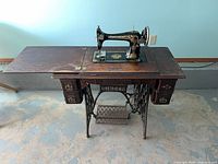 Full view of Singer treadle sewing machine in cabinet showing extension leaf, drawers and base