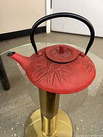 Full view of red cast iron teapot on glass table