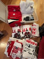 Overview of bin containing sweaters, scarf, T-shirts and rally towels