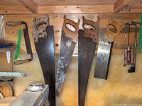 Five woodworking tools hanging: three full-size hand saws, one backsaw, one drawknife