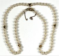Full view of pearl necklace showing length, pearls, gold heart accents, clasp, safety chain