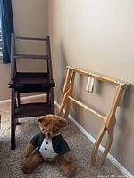 Dark wood folding step stool chair next to luggage rack and teddy bear