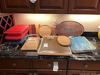 Overall lot on countertop showing bowls, baking dishes, lids, boards, mats, trivet, warming tray, sign