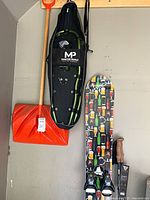 Snowshoes in bag hanging beside orange shovel and snowboard