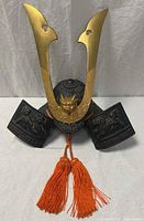 Full view of black kabuto helmet with brass crest and orange tassels