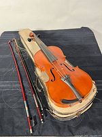 Violin on worn case with two bows showing missing hair and loose tailpiece